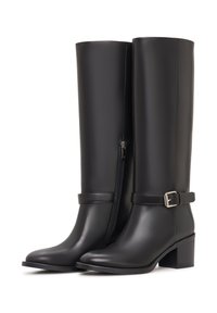 Musta nahkainen polven yläpuolelle ulottuva saapas, jossa on sileä pinta, sivuvetoketju ja koristellinen solkisilmukka nilkan kohdalla. Neliönmuotoinen korko.