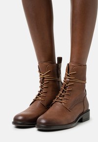 Bottes basses en cuir marron avec un bout arrondi, un laçage à l'avant et une fermeture éclair latérale. Dotées d'un petit talon empilé et de détails de couture minimalistes.