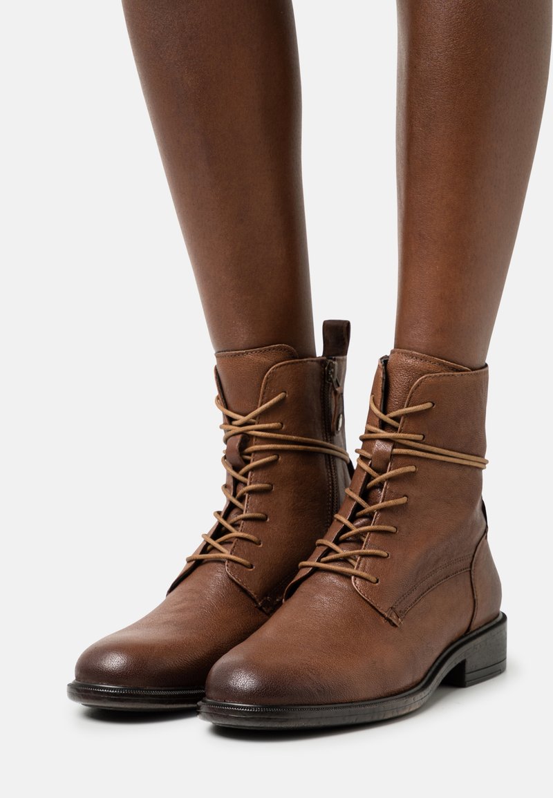 Bottes basses en cuir marron avec un bout arrondi, un laçage à l'avant et une fermeture éclair latérale. Dotées d'un petit talon empilé et de détails de couture minimalistes.
