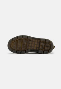 Black rubber shoe sole with a rugged, textured pattern and deep grooves for traction, featuring a translucent midsection and yellow accent.