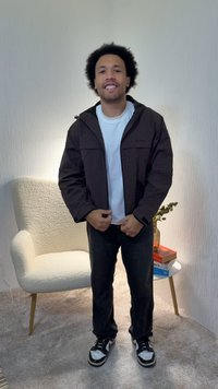 Black checkered jacket with a zip closure, relaxed fit, worn over a white t-shirt, paired with dark jeans and black and white sneakers.