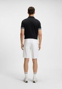 Polo shirt nero con strisce bianche sulle maniche, abbinato a pantaloni corti bianchi. I calzini presentano il logo "BOSS", indossati con sneakers di colore neutro.
