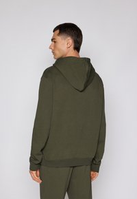 Fleece verde escuro com um bolso canguru, capuz com cordão e punhos canelados. Tecido macio com um corte descontraído, mostrado de costas.