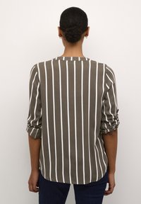 Blusa a rayas verdes y blancas con cuello redondeado, mangas enrolladas y dobladillo curvo. Fabricada con tejido ligero.