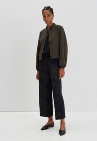 Olive green cropped jacket with button closure, paired with navy blue patterned wide-leg pants. Black flat shoes complete the outfit.