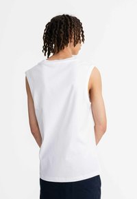 Witte mouwloze t-shirt van katoen, met een ronde hals en een relaxte pasvorm. Achteraan zichtbaar is de gladde textuur en het eenvoudige ontwerp.