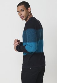 Ilgi piedurkņu džemperis ar horizontālām svītrām tumši ziliem, tirkīza un melniem toņiem, ar struktūrētu audumu un klasisku apaļu kakla izgriezumu.