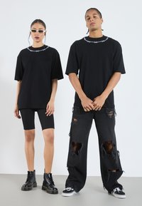 Camisetas negras de gran tamaño con un patrón de alambre de espino en el cuello, combinadas con jeans negros rotos y pantalones cortos negros ajustados, completadas con botas y zapatillas negras.