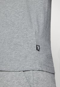 Grå kortærmet skjorte lavet af blødt bomuld. Har et side-seam-label med et sort logo og en glat tekstur. Kantene er let krummede.