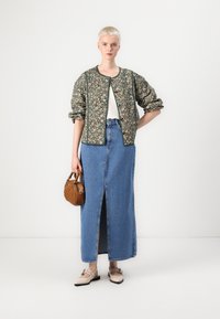 Bloemmotief gewatteerde jas, witte t-shirt, blauwe spijkerrok tot aan de enkel met een split aan de voorkant, bruine gevlochten handtas en beige ballerina's.