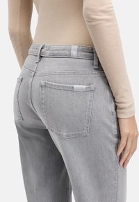 Szare jeansy z denimu o średnim stanie, wyposażone w tylne kieszenie oraz dyskretną metkę na pasie. Miękka tekstura i zwężany krój.