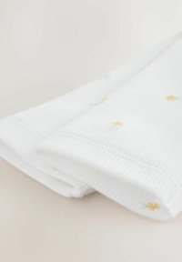 Vitt ribbat tyg med mjuk struktur, prytt med små gula och ljusblå blommönster. Vikta kanter synliga för detalj.