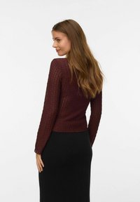 Burgunderfarvet, strikket top med lange ærmer og fitted design. Stoffet har teksturerede detaljer og en cropped længde, parret med en sort nederdel.