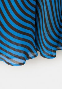 Tissu bleu transparent avec des rayures diagonales noires, s'étalant sur une surface blanche, montrant des plis doux et une légère transparence.