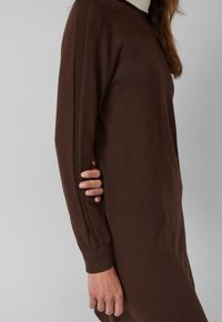 Robe en tricot marron à manches longues, avec des détails côtelés le long des épaules. Texture douce et forme légèrement ajustée.