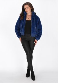Giubbotto bomber in pelliccia sintetica di colore blu navy con colletto alto, chiusura con zip davanti e due tasche laterali. Abbinato a pantaloni in finta pelle neri.