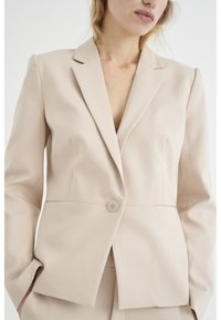 Krémový upravený blazer s klopovým límcem, zapínání na jeden knoflík, hladká textura a strukturovaný střih, navržený pro profesionální vzhled.