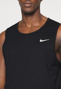 Débardeur noir sans manches Nike avec un col rond, arborant un logo blanc sur la poitrine. Fabriqué en tissu lisse et extensible.