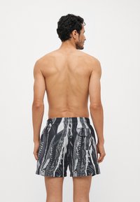 Shorts de bain pour hommes avec un motif abstrait noir et blanc, en tissu texturé, avec une taille élastique et une poche arrière.