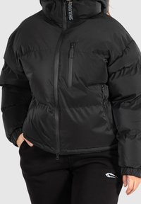 Giacca imbottita nera con colletto alto, cerniera frontale e numerose tasche con zip. Presenta una texture liscia e lucida e polsini a coste.