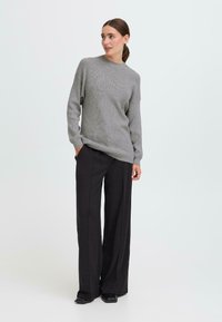 Grauer Strickpullover mit Rundhalsausschnitt, kombiniert mit schwarzen weiten Hosen. Das Outfit zeichnet sich durch eine lässige Passform und strukturierte Stoffe aus.