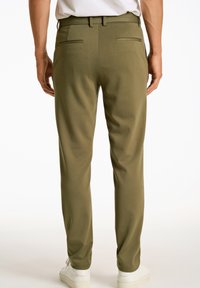 Olijfgroene broek met een slim fit en een gladde textuur. Voorzien van twee achterzakken en een riemlus, gecombineerd met witte sneakers.