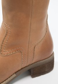 Bottines en cuir marron avec des coutures décoratives, un talon texturé et un design à bout rond. Fini lisse avec une surface mate.