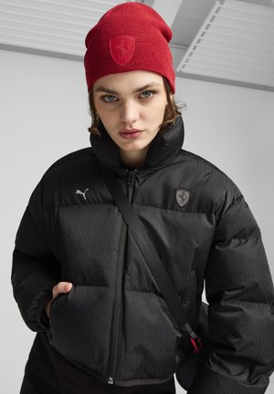 Czarna puchowa kurtka z subtelnym wzorem, wysoki kołnierz, srebrne logo Puma. Czerwona dzianinowa czapka z wytłoczonym logo. Czarny pasek przebiegający przez ciało.