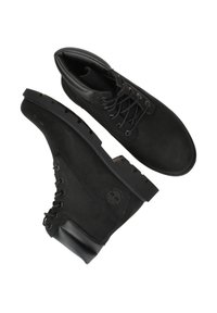Black ankle boots made of suede and leather with lace-up closure, textured detailing on the sides, and a durable rubber sole.