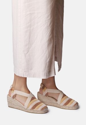 Voeten met beige en bruin gestreepte espadrille sleehakken met enkelbandjes, gecombineerd met lichtgekleurde enkelhoge broek.