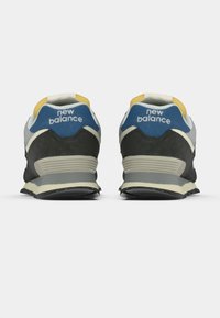 Fekete és szürke sneaker cipők kék és sárga árnyalatokkal, párnázott sarokkal, texturált anyagokkal és egy jellegzetes logóval a hátulján.