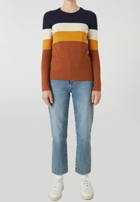 Stickad tröja med lång ärm i randigt i marinblått, kräm, senap och rostfärg; ihop med ljusblå jeans och vita sneakers.