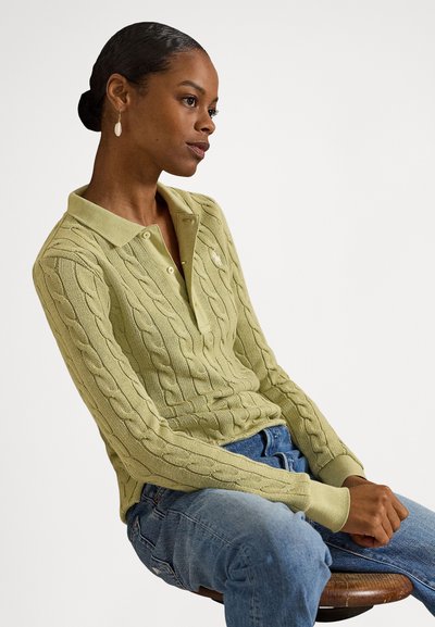Svetlo zelena pletena polo majica z vzorci v obliki kabel, ovratniškim dizajnom in tremi gumbi. Nosi se z modrimi denim kavbojkami.