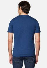 Granatowa bawełniana koszulka z krótkim rękawem, okrągłym dekoltem i małym logo marki na karku. Połączona z ciemnymi dżinsami.