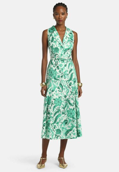 Woman wearing sleeveless, green and white floral-patterned midi dress with collar and belt, gold bracelets, and gold pointed flats.