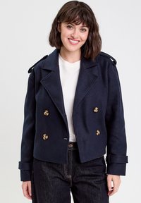 Veste en laine bleu marine croisée avec des boutons dorés, revers en pointe et épaulettes ; design court avec des manches à revers.