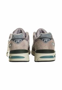 Sneakers New Balance con una toma grigia in suede, dettagli in rete e una suola bicolore con un accento color acquamarina. Numero di modello 'V2' sul tallone.