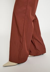 Roestkleurige, wijd uitlopende broek van gestructureerde stof, met een rechte snit en een gespleten zoom, gedragen met beige puntige hakken.