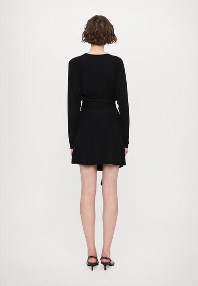 Svart långärmad klänning med figurnära överdel och utsvängd kjol. Mjukt tyg, slät struktur. Matchad med svarta, remmade klackskor.