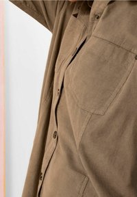 Camicia in corduroy marrone con design a bottoni, due tasche sul petto e vestibilità rilassata, caratterizzata da una fine trama a coste e bottoni metallici.
