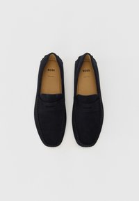 Mustad mustad loafers madal profiiliga, õmblustega detailid ja sile viimistlus. Interjööril on pruun nahksool. "BOSS" bränding on nähtav.
