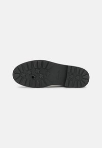Suela de zapato de goma negra con una superficie estriada. Presenta patrones de tracción en forma de estrella y un borde liso. Se aprecia la marca estampada.