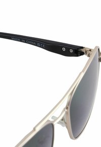Metalen zonnebril met grijze lenzen, voorzien van een slank zilveren montuur en een zwarte arm. Inclusief een zilveren scharnier en een merklabel met de tekst "Made in China."