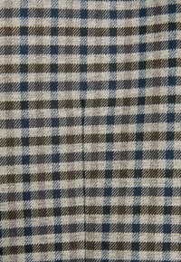 Textilie s kostkovaným vzorem; barvy zahrnují krémovou, hnědou a námořnickou. Materiál se jeví jako texturovaný s tkaným pocitem.