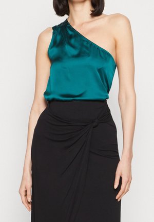Femme portant un top en satin bleu canard à une épaule, associé à une jupe noire taille haute avec un détail en nœud à l'avant.