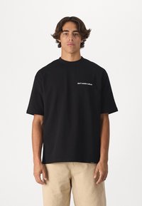 Camiseta negra de manga corta hecha de algodón, con el texto blanco "no desperdicies la cultura" en el pecho. Diseño simple y relajado.