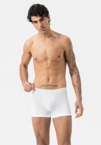 Shorts en coton blancs avec une texture lisse et une taille élastique, portés par un mannequin masculin tatoué, sur un fond neutre.