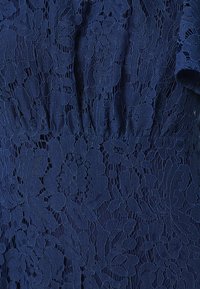 Marinblå blondekjole med et blomstermotiv og fine detaljer. Materialet er gennemsigtigt med en struktureret overflade og en indsnævret talje.