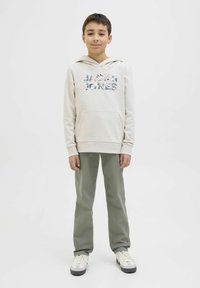 Gai krems krāsas kapuce džemperis ar ziedu "Jack & Jones" logo, apvienots ar olīvzaļiem biksēm un baltiem sporta apaviem. Gluda tekstūra, ikdienišķs piegriezums.