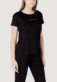 T-shirt nera in cotone con maniche corte, caratterizzata da un design semplice e dalla scritta dorata "ARMANI EXCHANGE" sul petto.